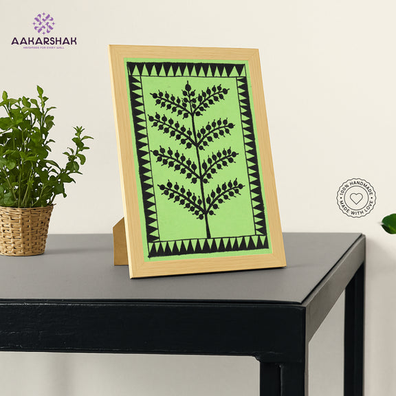 Framed artwork with green background and black tree warli painting
